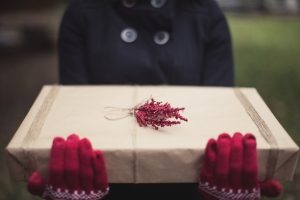 A woman wearing red gloves holding a gift wrapped in brown paper - 5 Great Gifts To Give Yourself This Christmas - Sandra Harewood Counselling