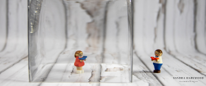 Female Lego Toy In Glass Container With Male Lego Toy The Other Side of The Glasswork Looking In - How To Stay Connected When Social Isolating COVID19 - Sandra Harewood Counselling