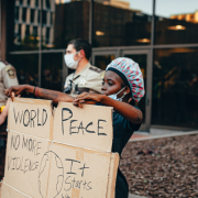 Why Racism Is Like Being In An Abusive Relationship – Sandra Harewood Counselling Black Woman Holding Cardboard Banner With World Peace Written On It Surrounded By White Policemen- Why Racism Is Like Being In An Abusive Relationship - Sandra Harewood Counselling