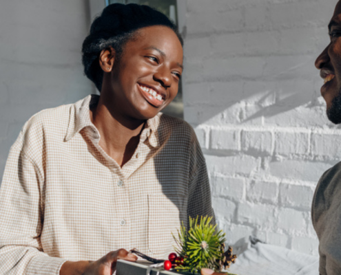 A happy black couple with a woman handing her boyfriend a gift. Couples counselling works by helps creating healthy relationships - Sandra Harewood Counselling