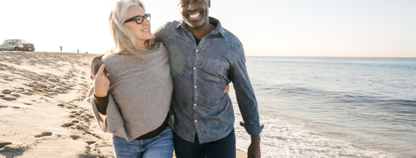 Couple mixed race couples walking hand in hand on the beach, symbolising connection and harmony in their relationship.