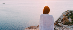 Woman sitting on a cliff edge looking out on the ocean - Unlocking the Benefits of Emotional Awareness in Relationships - Sandra Harewood