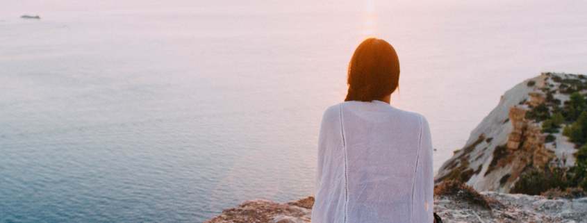 Woman sitting on a cliff edge looking out on the ocean - Unlocking the Benefits of Emotional Awareness in Relationships - Sandra Harewood