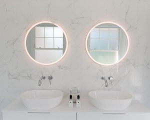 Two mirrors above twin wash basins reflecting softly lit surroundings, symbolising self-reflection, projection, and the challenge of truly seeing in relationships.