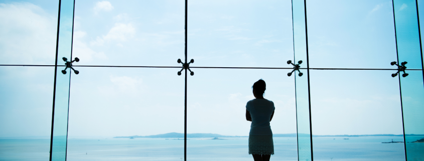 Woman looks of a window to the ocean - At a Relationship Crossroads? Why This Moment Deserves Care, Not Crisis