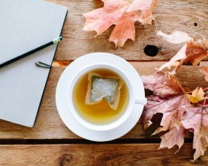 A cup of herbal tea on a table beside a journal with autumn leaves, inviting reflection and quiet contemplation