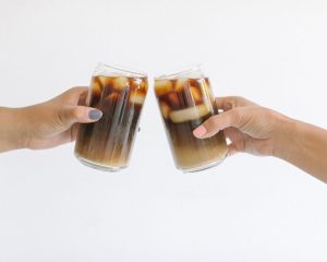 Two women gently tapping glasses filled with soft drinks, symbolising connection and mindful alternatives to alcohol and problem drinking