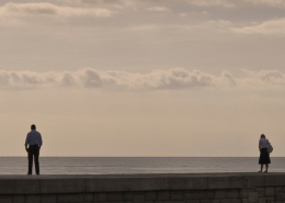 Couple standing apart looking out to sea, one partner wants to stay while the other feels unsure about the relationship