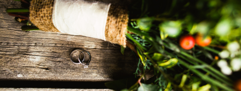 Wedding rings beside a bridal bouquet on a table in a vintage barn